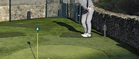 Un campo de golf con un putting green, un marcador de bandera y un muro de piedra.