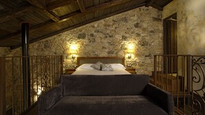 Un dormitorio con pared de piedra, vigas de madera, una cama con almohadas y dos lámparas de pared.