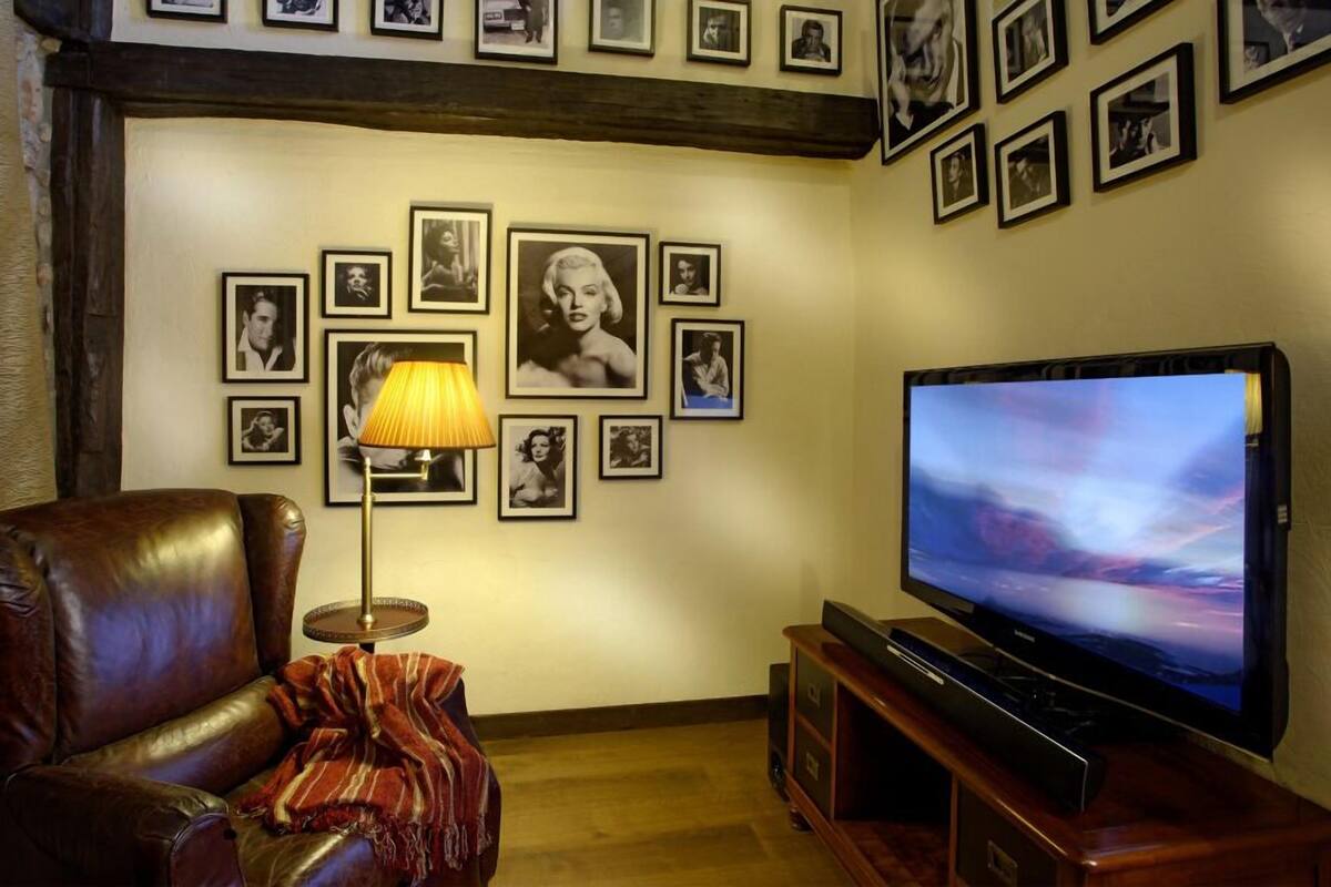 A living room with a leather sofa, a TV on a wooden stand, and a wall decorated with framed pictures.