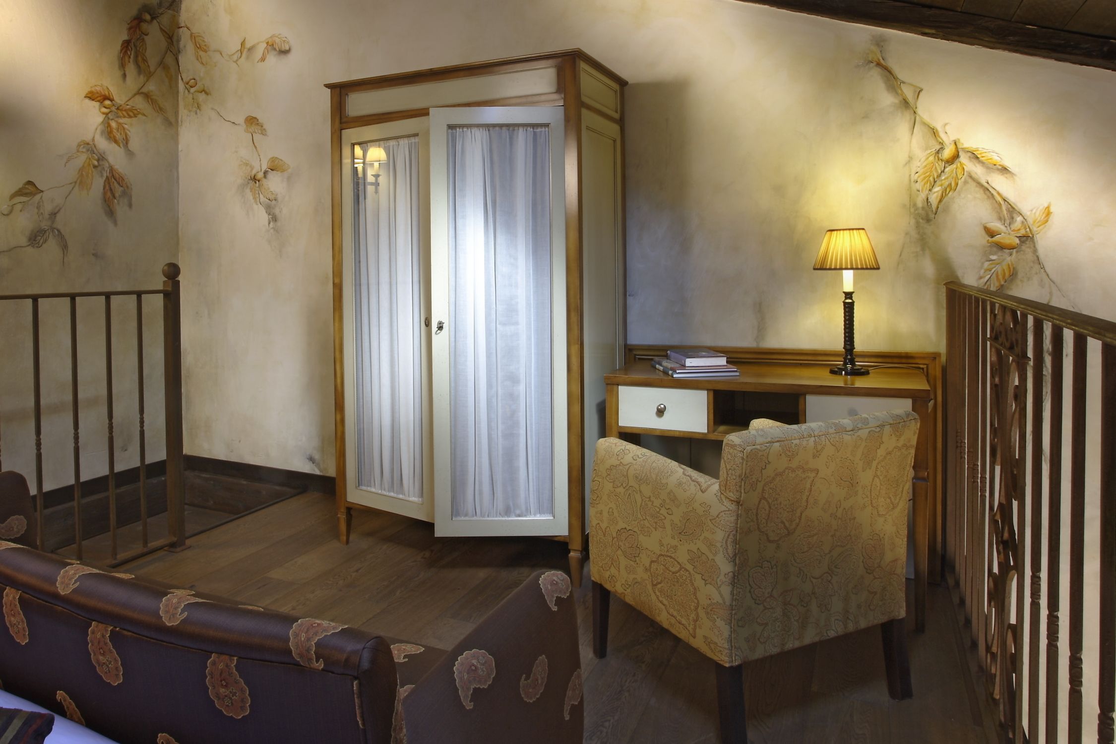 A room with a wooden desk, a chair, a wardrobe, and a lamp.
