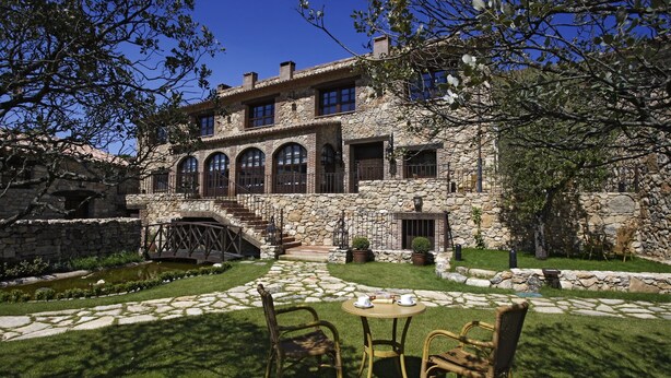 Un edificio de piedra con patio, un pequeño puente y un estanque.
