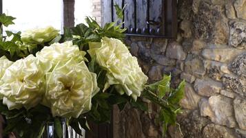 A table with a clear glass vase containing white flowers, set against a stone wall with a rustic wooden door.