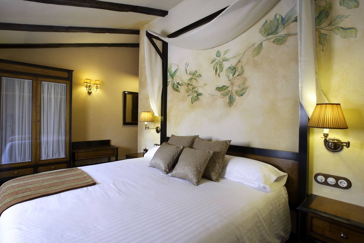 A neatly made bed with multiple pillows, a bedside lamp, a nightstand, and a wall-mounted lamp.