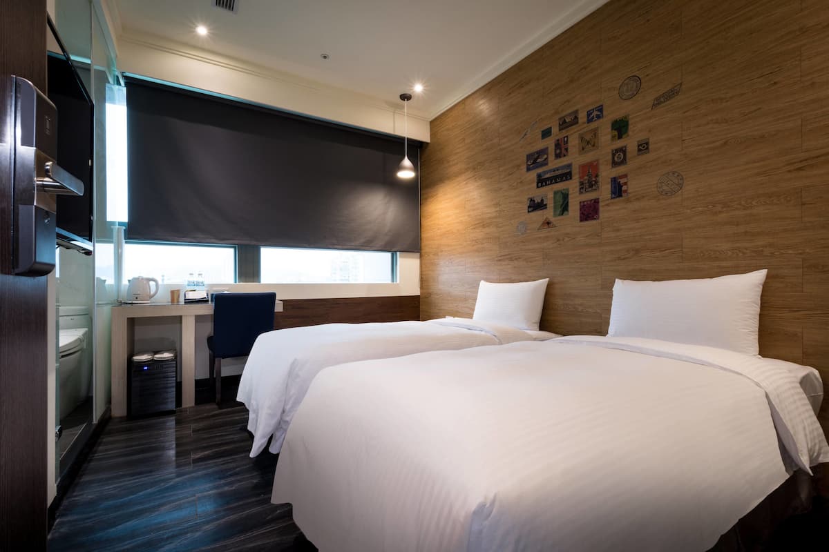 A hotel room with two beds, a desk, a chair, and a large window.