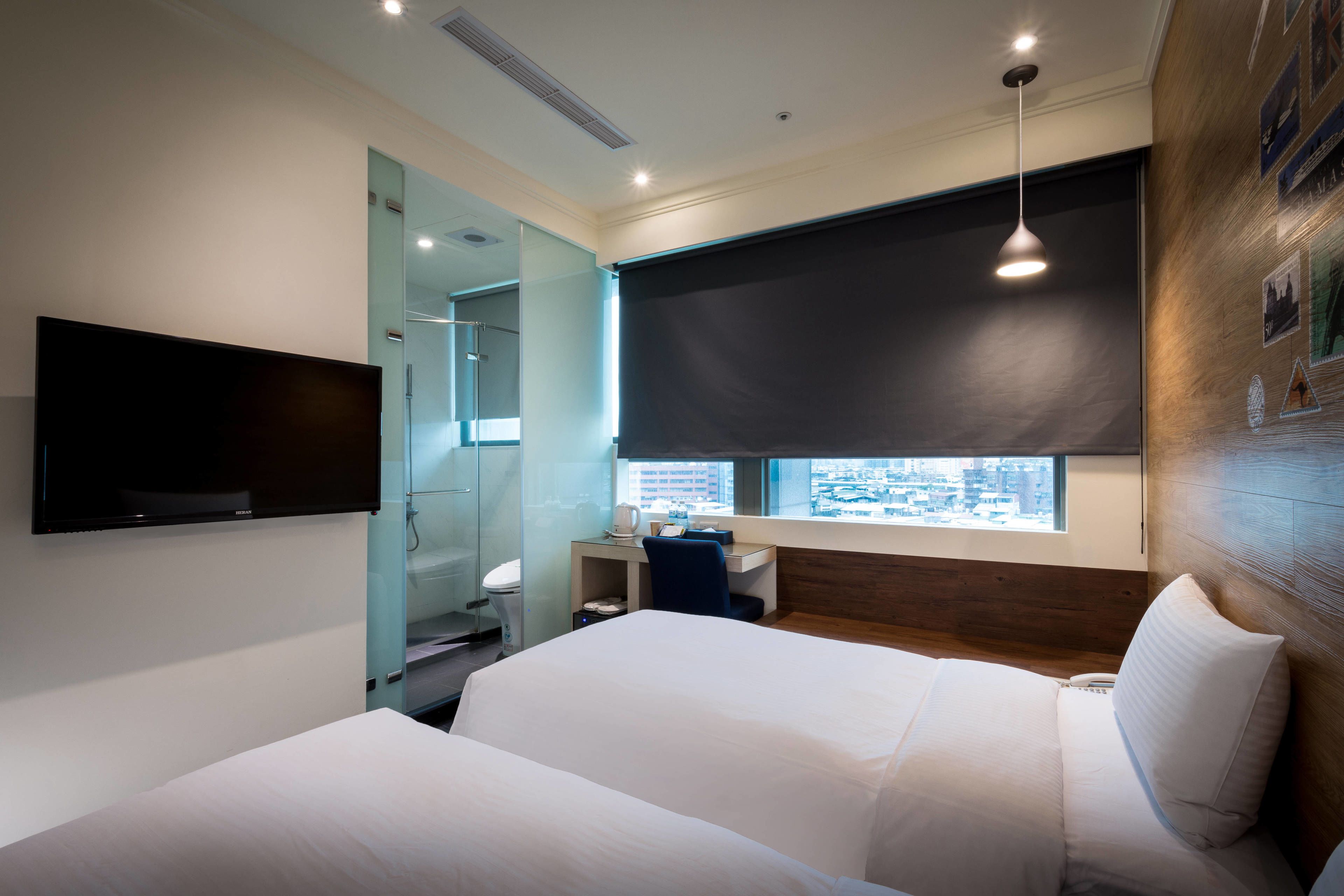 A modern hotel room with a large bed, a desk, a flat-screen TV, and a window with a city view.