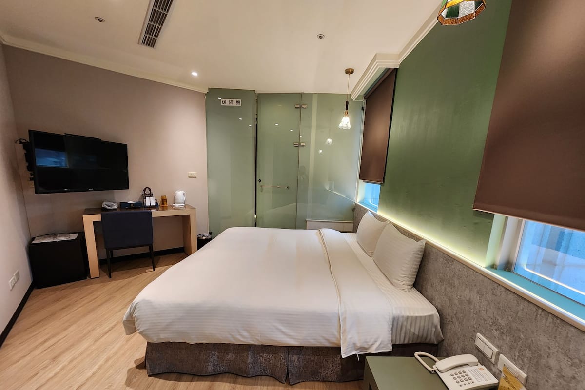 A hotel room with a bed, a desk with a telephone, a television, and a glass-enclosed shower area.