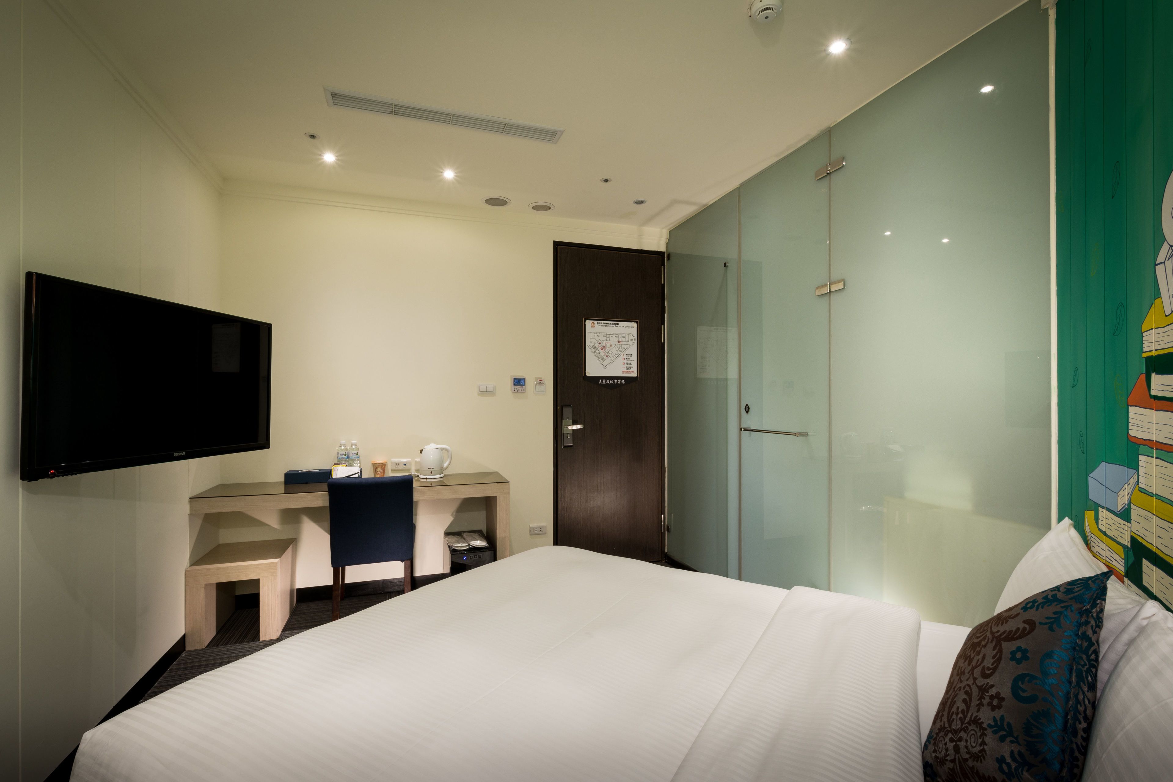 Una habitación de hotel con cama, escritorio, silla, televisor y armario.