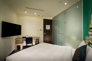 Una habitación de hotel con cama, escritorio, silla, televisor y armario.