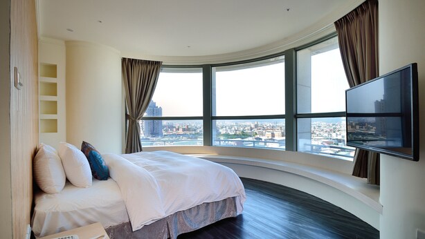 A modern hotel room with a curved bed, a flat-screen TV, and a city view through large windows. - Merryday Hotel Banqiao Branch (New Taipei City)