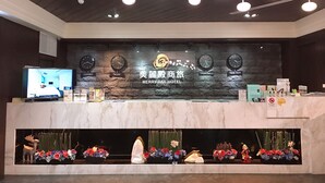 A hotel reception area with a stone wall, clocks indicating different cities, a TV screen, and a floral display. - Merryday Hotel Banqiao Branch (New Taipei City)