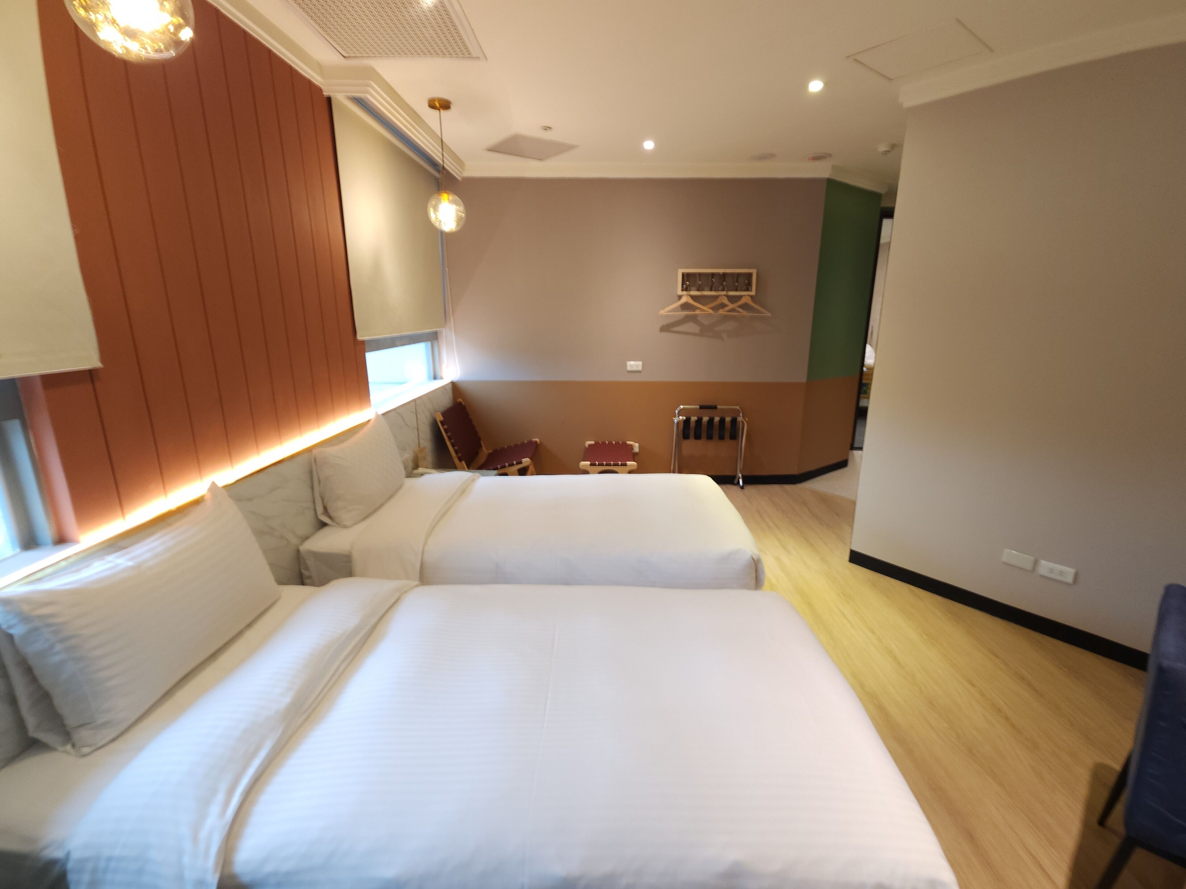 Habitación de hotel con dos camas, cabecera de madera, zona de estar con sillas y una pequeña mesa.