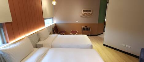 Habitación de hotel con dos camas, cabecera de madera, zona de estar con sillas y una pequeña mesa.