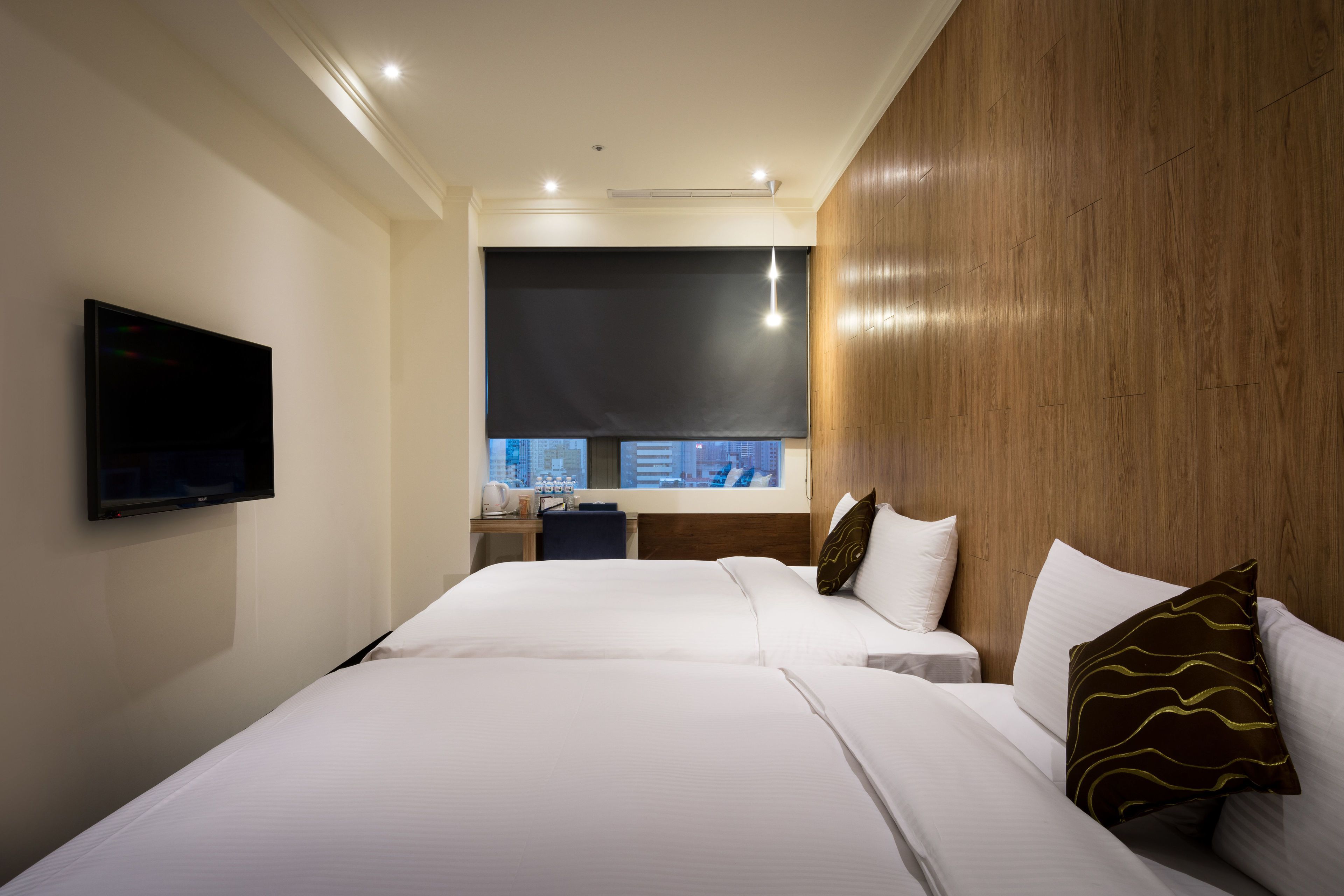 Habitación de hotel con dos camas, un televisor, una ventana con vista a la ciudad y cabecero de madera.