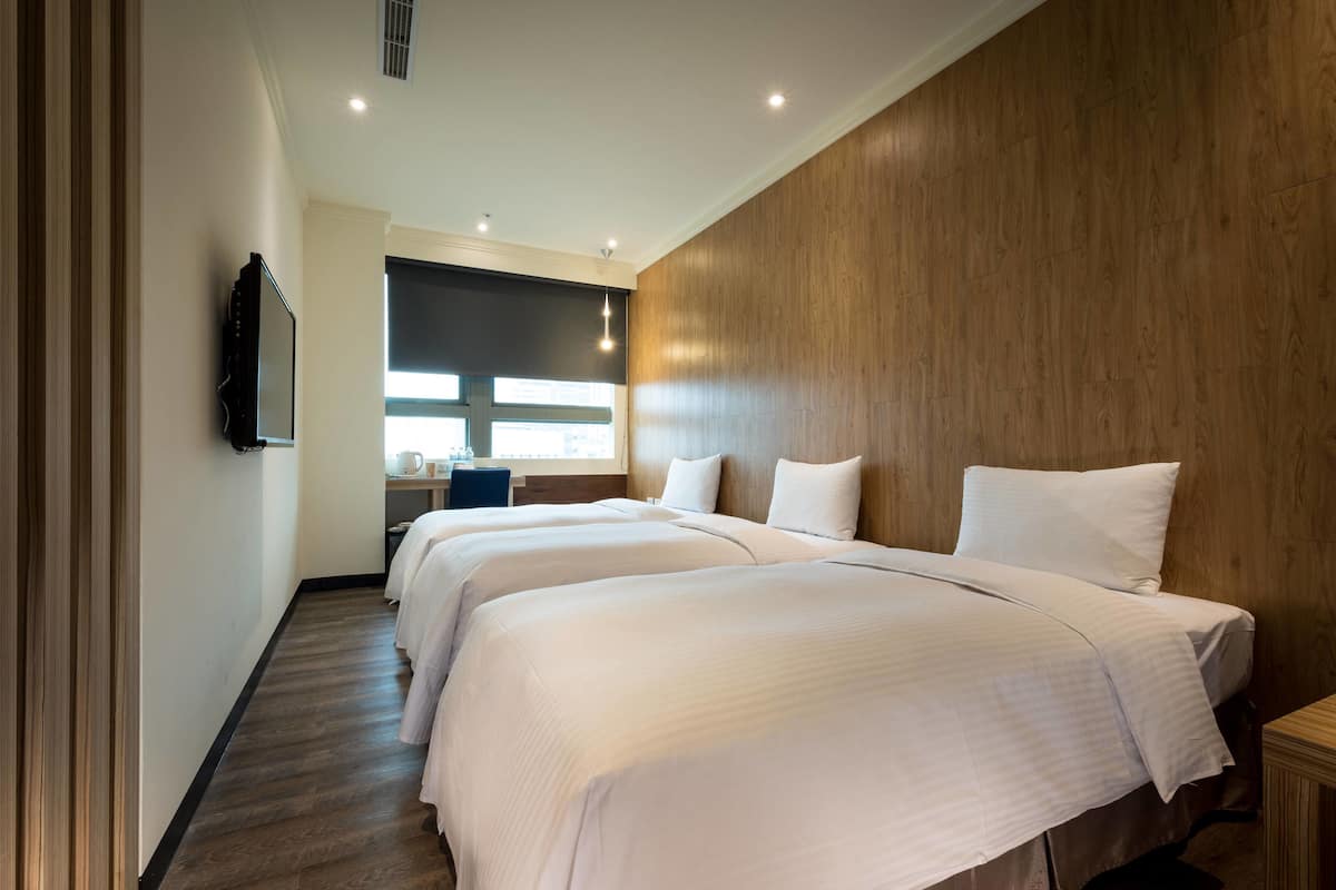 A hotel room with three beds, a wooden accent wall, a flat-screen TV, and a desk with a chair.