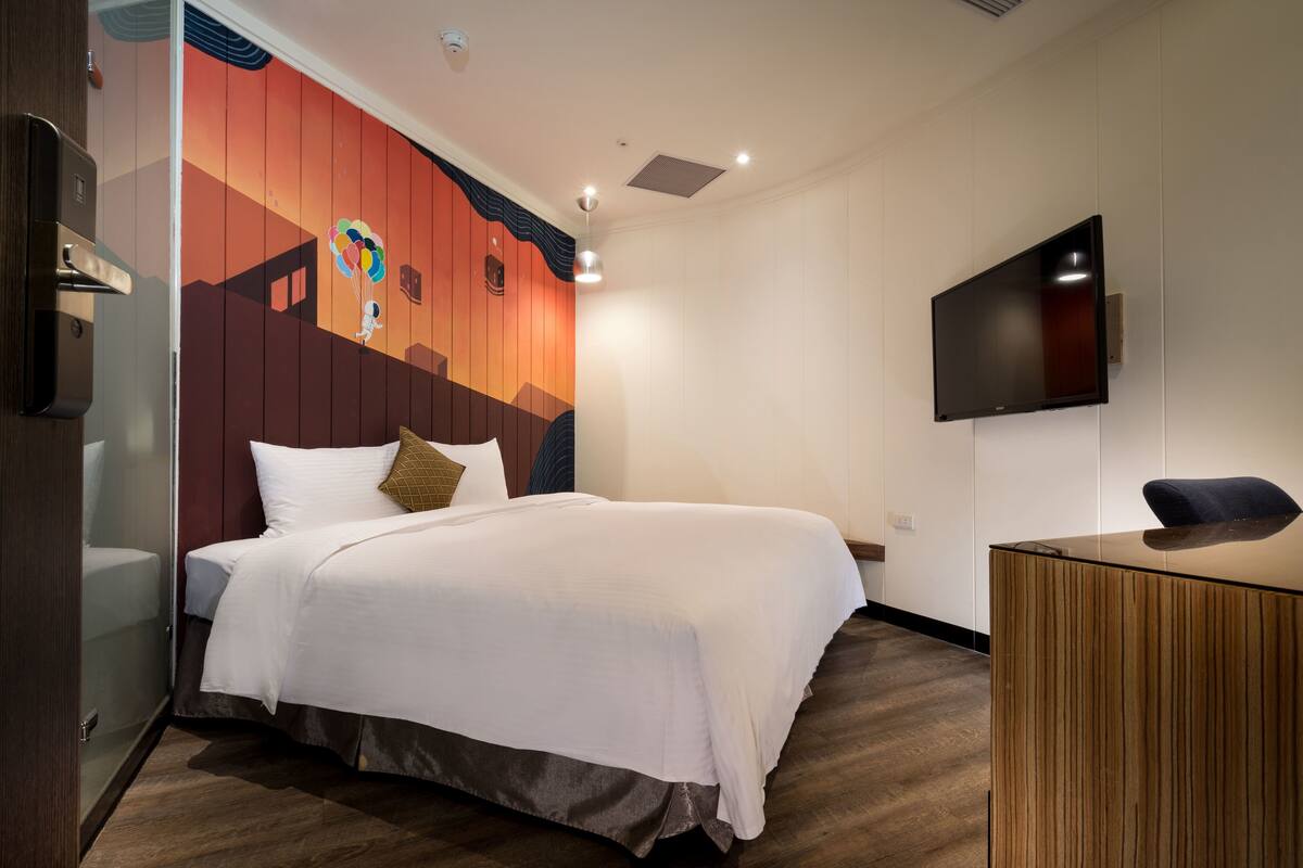 A hotel room with a bed, a desk, a television, and a wall with a colorful mural.