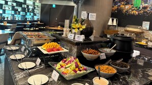 A buffet area with various food options and a television screen displaying a cityscape. - Merryday Hotel Banqiao Branch (New Taipei City)