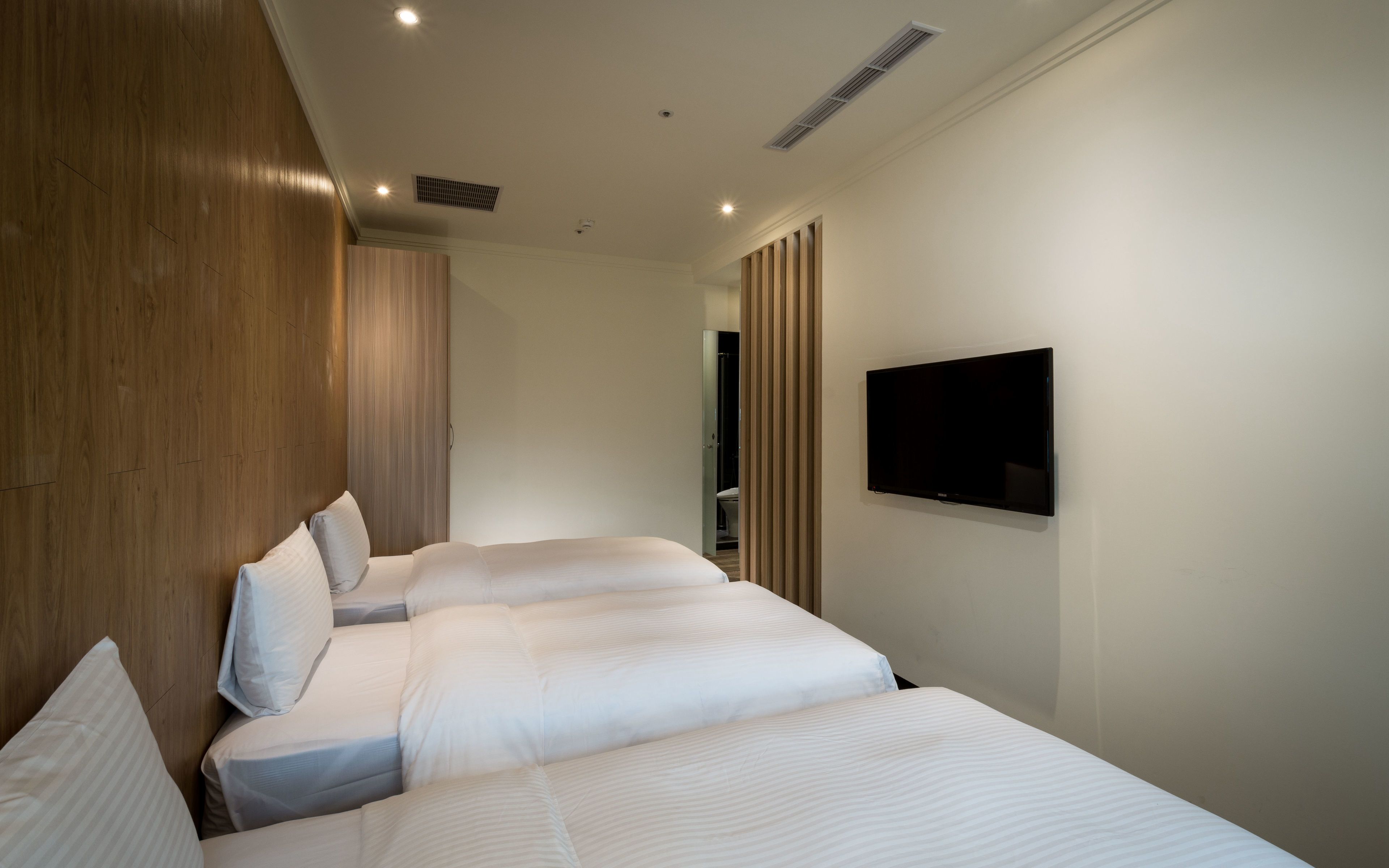 A modern hotel room with two beds, a flat-screen TV, and a wooden panel wall.