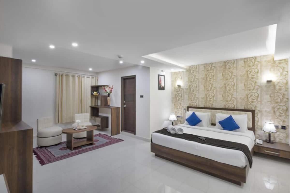 A hotel room with a bed, bedside tables, a desk, a chair, and a television.