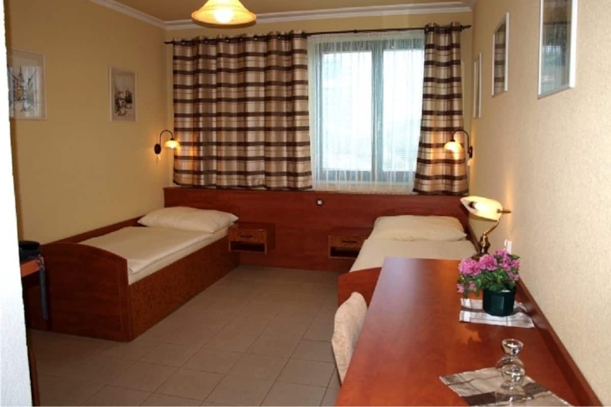 Ein Zimmer mit zwei Holzbetten, einem Holztisch, einem Fenster mit Vorhängen, Wandlampen und gerahmten Bildern an der Wand.
