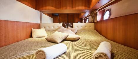 A hotel room with a striped bedspread, a tufted headboard, and two rolled towels on the bed.