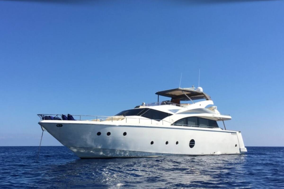 Un grand yacht blanc, doté de plusieurs ponts et d’un pont supérieur couvert, voguant sur des eaux bleues et calmes.