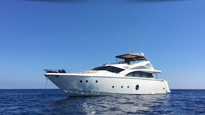 Un grand yacht blanc, doté de plusieurs ponts et d’un pont supérieur couvert, voguant sur des eaux bleues et calmes.