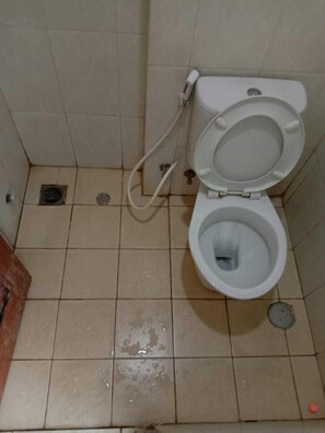 Un baño pequeño con azulejos, un inodoro, un desagüe visible y un rociador bidet.