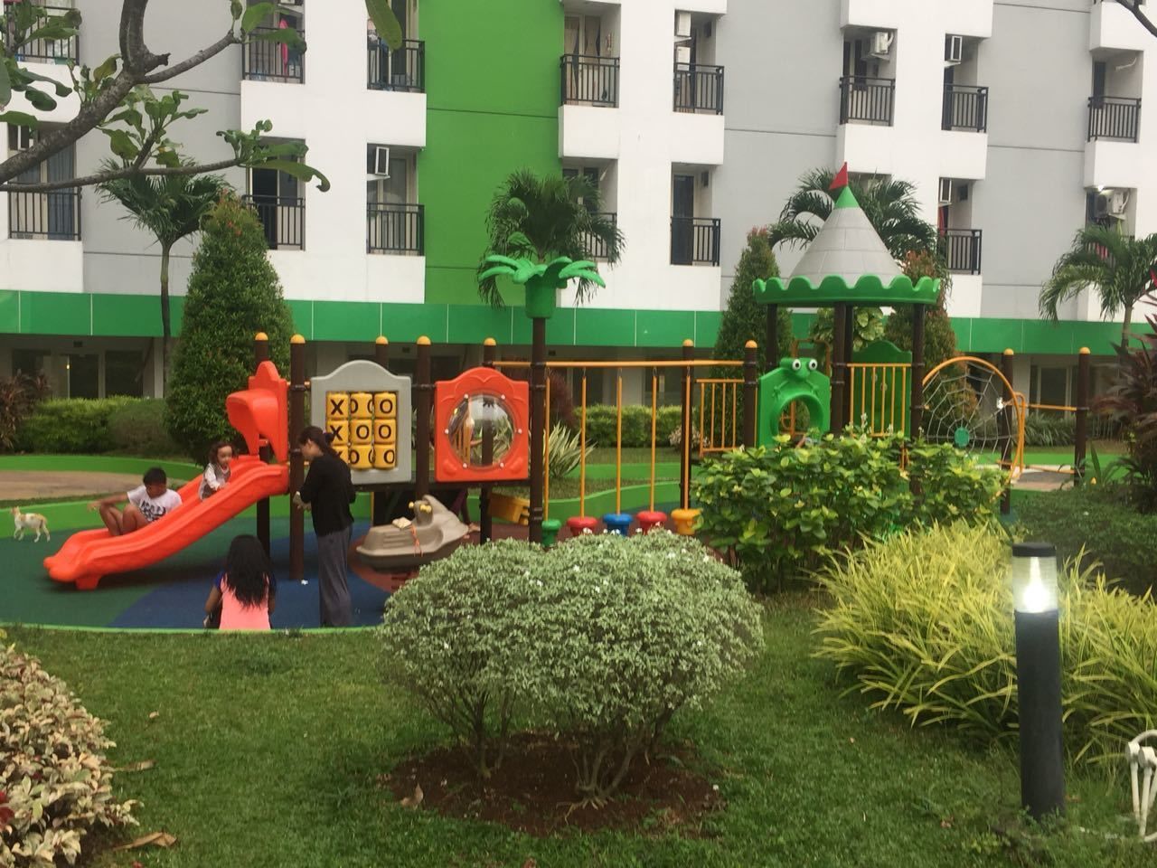 A playground with slides and climbing structures, surrounded by greenery and a building with balconies.