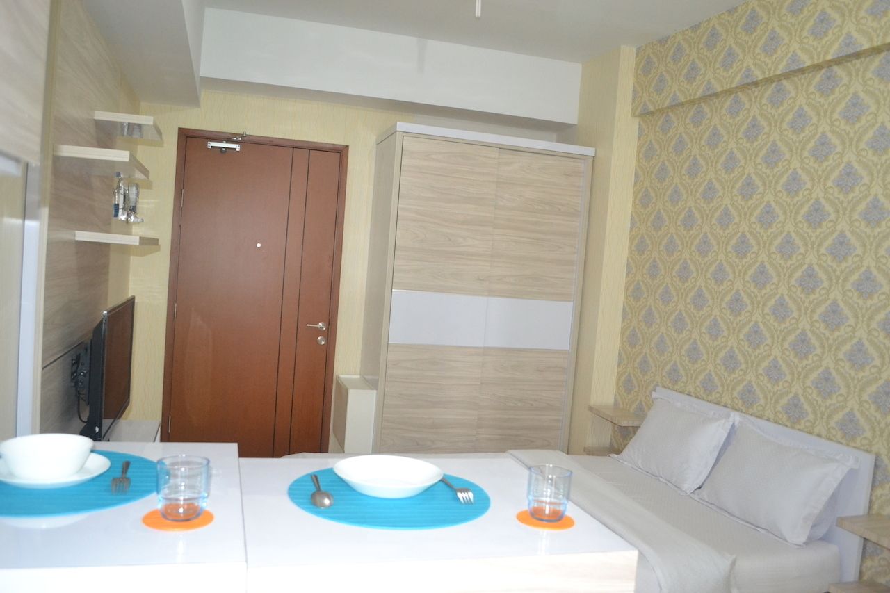 A hotel room with a double bed, a TV, a wardrobe, and a bathroom with a shower and sink.