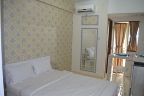Habitación de hotel con cama, una mesita con espejo, inodoro y un equipo de aire acondicionado en la pared.