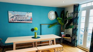 A dining area with a wooden table and benches, a large plant, and a wall-mounted clock. - Pebble Mews Free Parking | By My Getaways (Brighton)