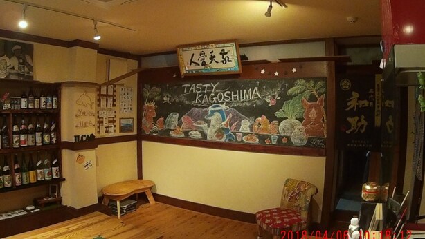 A cozy restaurant interior with a chalkboard menu, wooden furniture, and a variety of bottles on shelves. - KAGOSHIMA ILCA GUEST HOUSE - Hostel (Kagoshima)