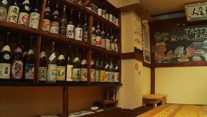 A bar area with shelves of bottles, a chalkboard menu, and a wooden counter. - KAGOSHIMA ILCA GUEST HOUSE - Hostel (Kagoshima)