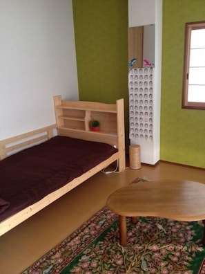 Ein kleines Zimmer mit einem Einzelbett, einem runden Tisch und einem gemusterten Teppich.