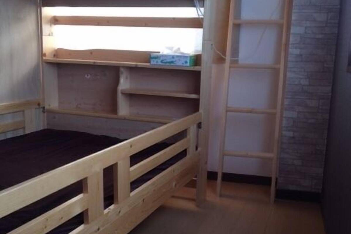 Un lit superposé avec une échelle, une petite étagère et une boîte étiquetée « Gek ».