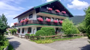Un bâtiment à deux étages, doté de balcons ornés de fleurs, d’une clôture en bois à l’avant et surplombant un ciel dégagé.