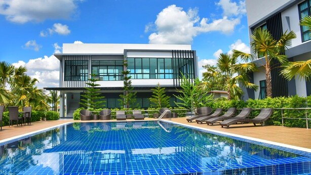 A modern hotel with a swimming pool, lounge chairs, and palm trees. - Eireann Boutique Hotel (Prakhon Chai)
