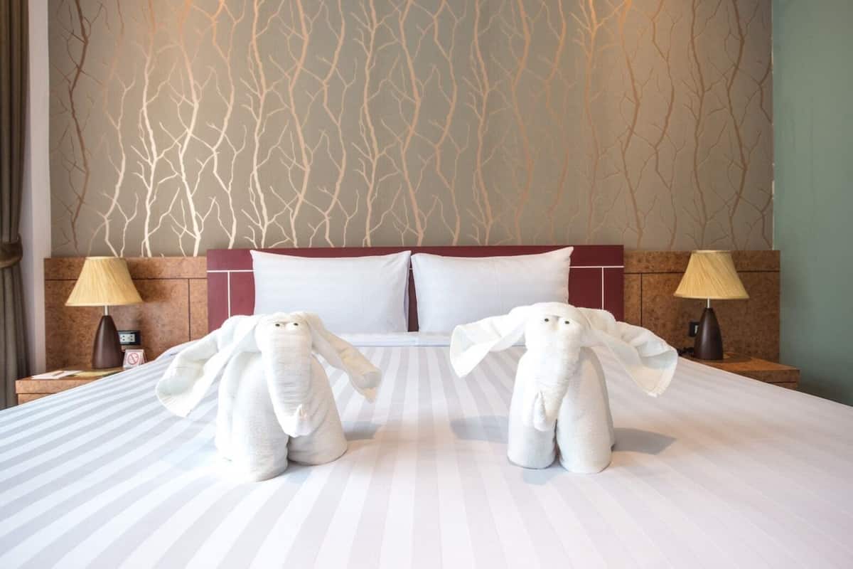 Une chambre d’hôtel avec un grand lit, deux tables de chevet avec des lampes et un mur orné d’un motif représentant une branche d’arbre.