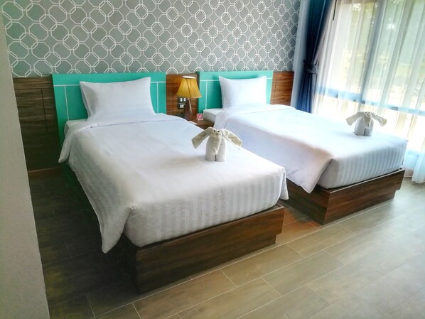 Two neatly made beds with white linens and pillows, a wooden headboard, a lamp on a nightstand, and a patterned wall.