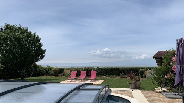 Una piscina con cerramiento de vidrio, sillas de descanso rojas y vista al mar.