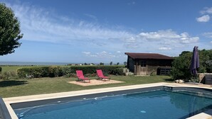 Una piscina con dos sillas reclinables rojas y una cabaña de madera al fondo.