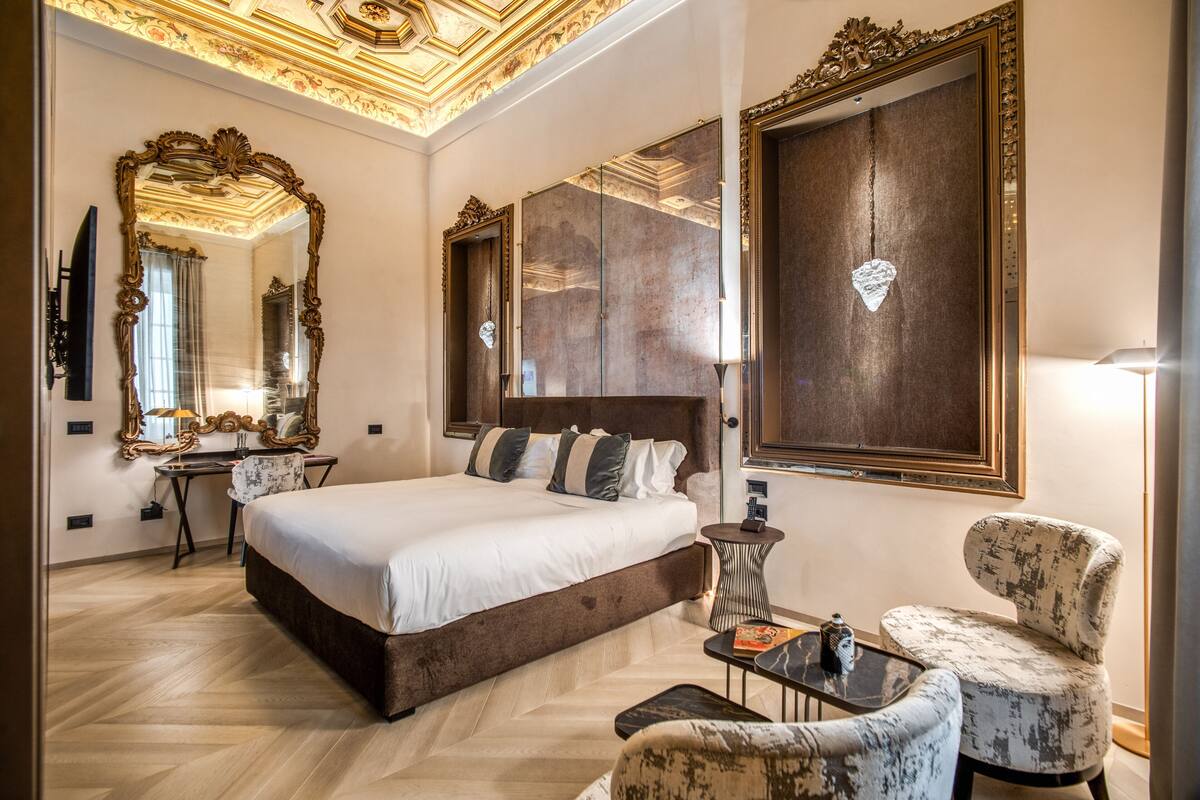 A spacious bedroom with a large bed, a desk, a chair, and a mirror.
