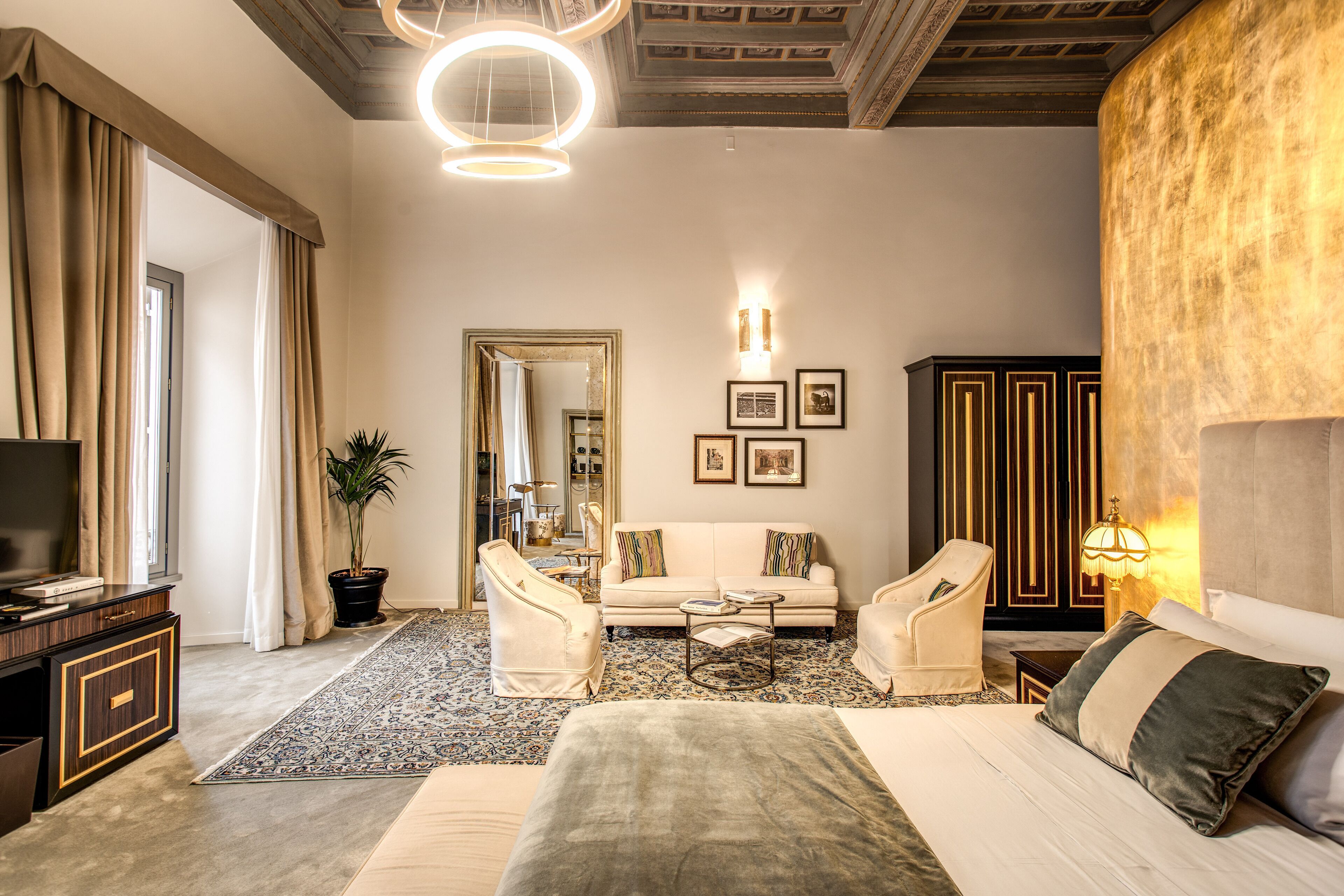 A spacious hotel room with a large bed, two armchairs, a sofa, a coffee table, a TV, and a large mirror.