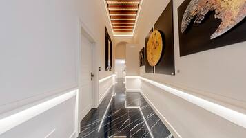 Um corredor moderno com piso de mármore preto, paredes brancas e teto com iluminação embutida.