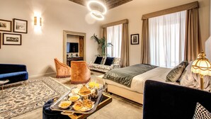 Habitación de hotel con cama, sofá, mesa de comedor con desayuno, espejo y techo con detalles decorativos.