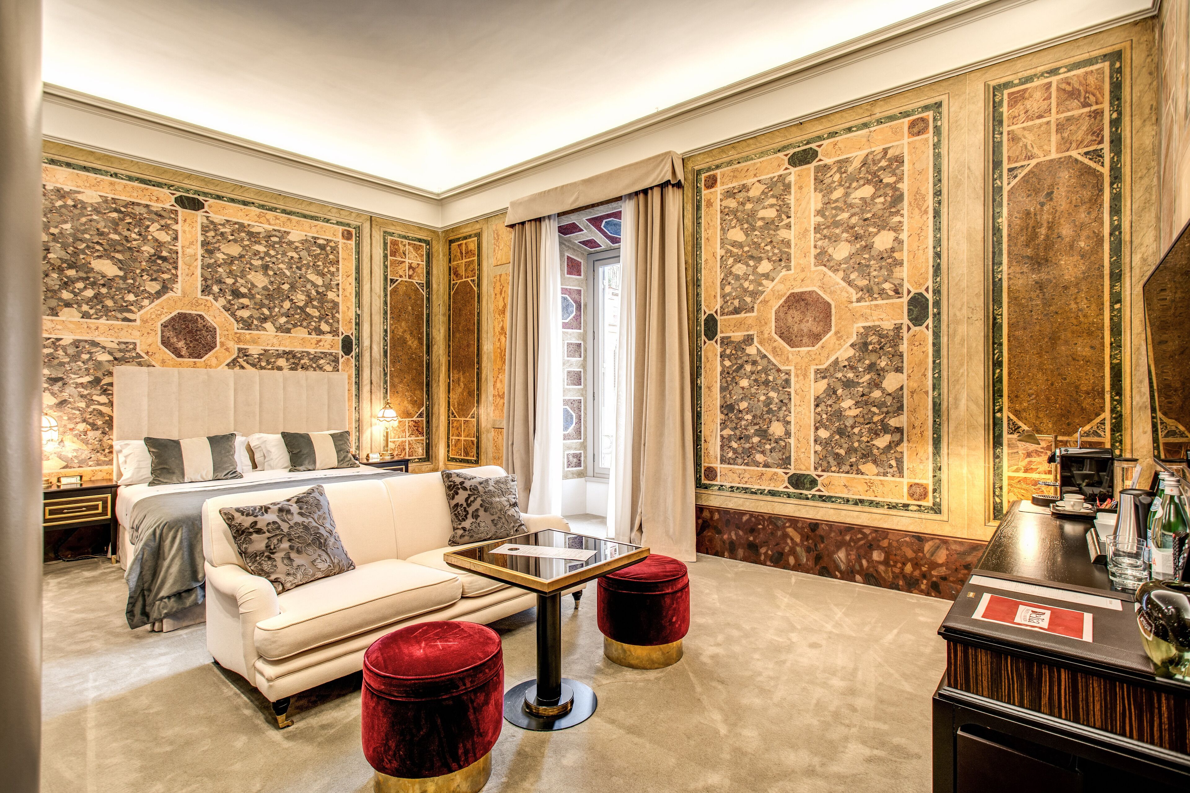 A luxurious room with a large bed, a sofa, a small table, and two red ottomans.