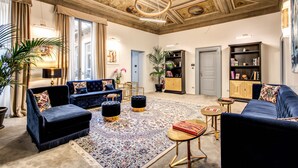 Un salón espacioso con un amplio sofá azul, un tapete estampado y un techo con molduras decorativas.