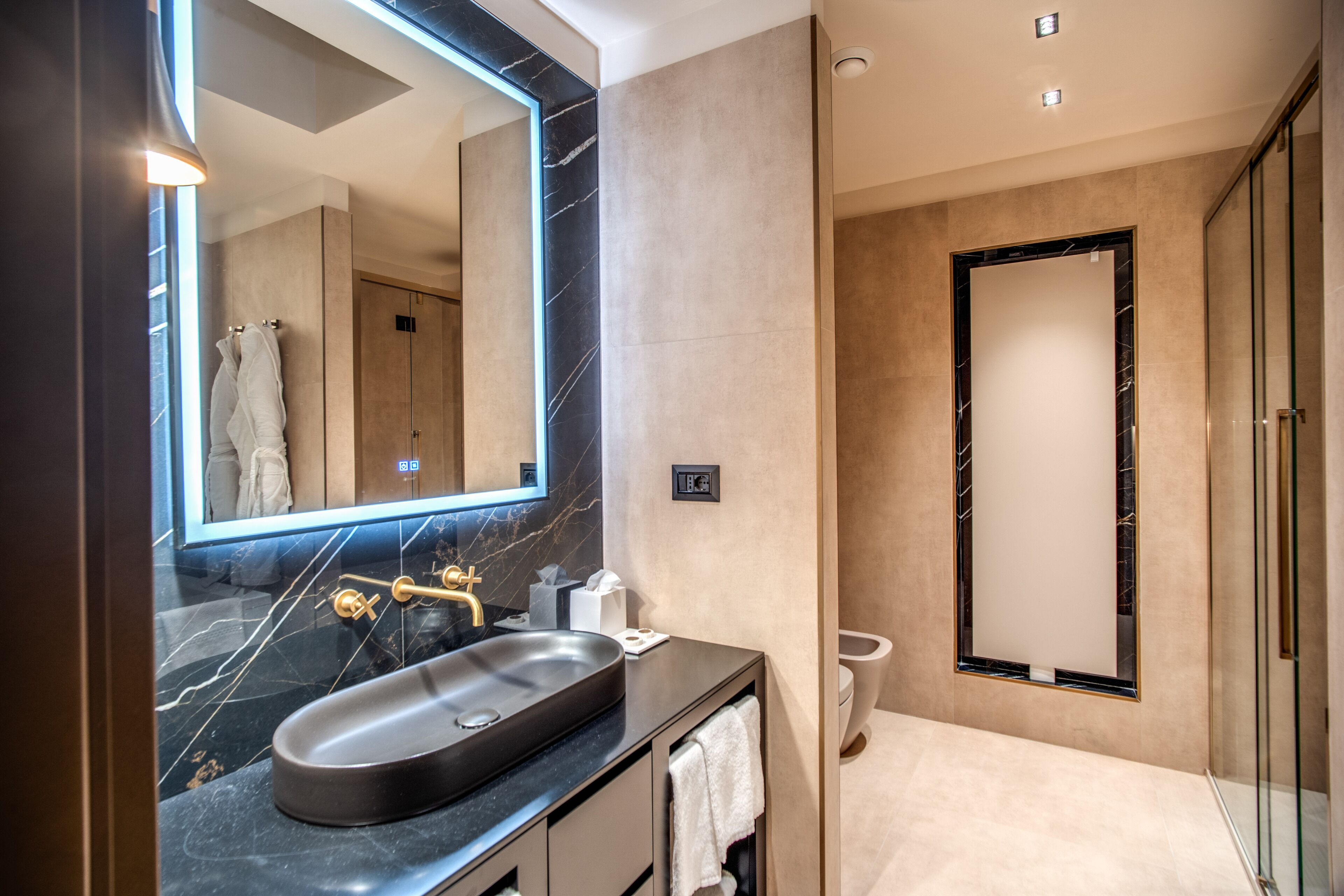 Un baño moderno con un espejo grande, un lavabo negro y una cabina de ducha con paredes de vidrio.