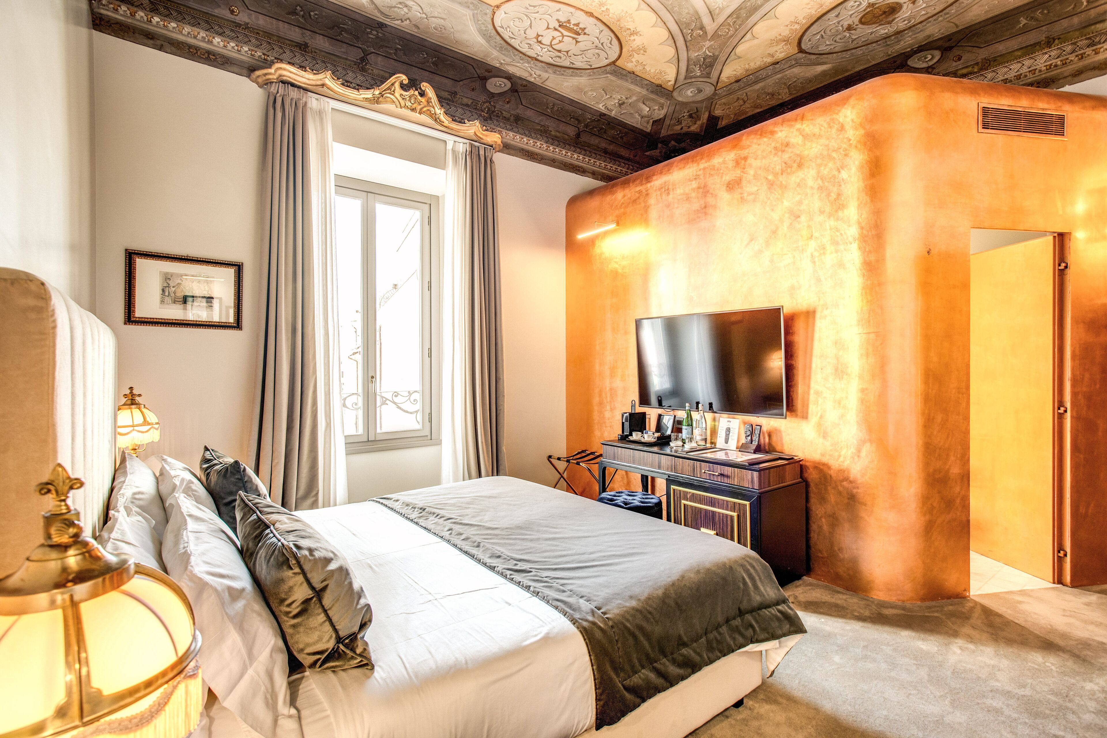 Habitación de hotel con cama, escritorio con televisor de pantalla plana, ventana con cortinas y techo decorativo.