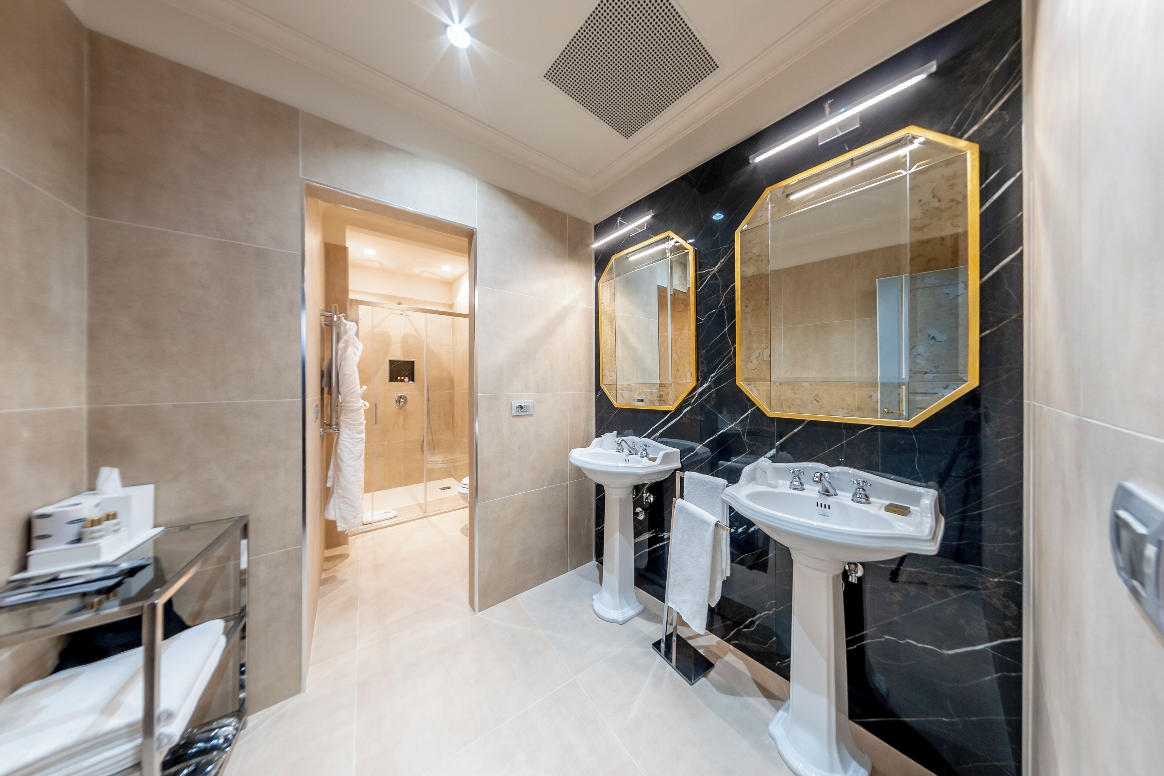 Un baño moderno con dos lavamanos, cabina de ducha de vidrio y paredes de mármol.